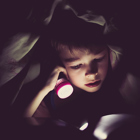 Pojke läser bok under täcket med ficklampa